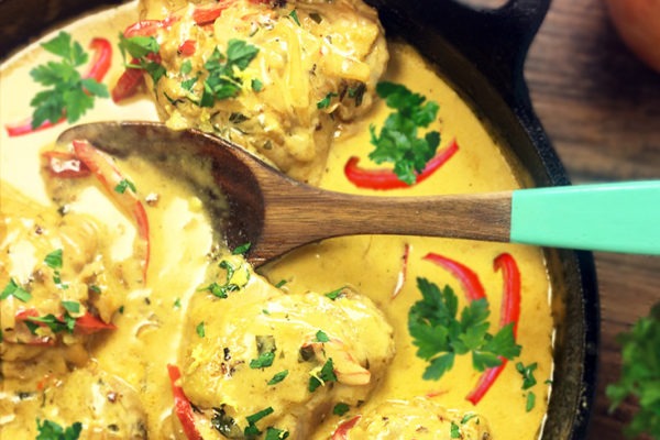 Curried Chicken Thighs in a cast iron skillet simmering in heavy cream sauce with onions, red bell pepper slices, and parsley.